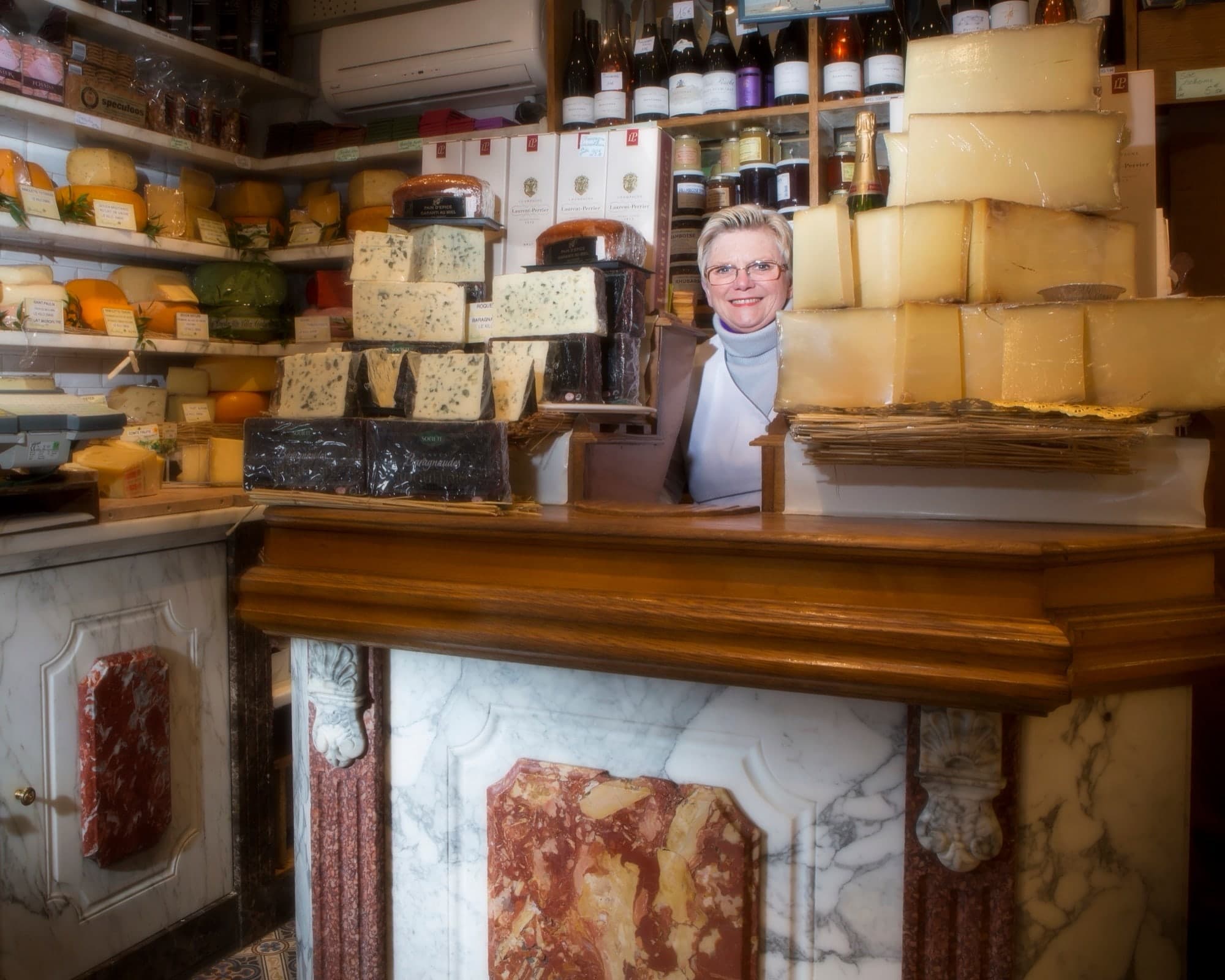 Portrait d'une fromagère derrière son comptoir en marbre entouré de fromages