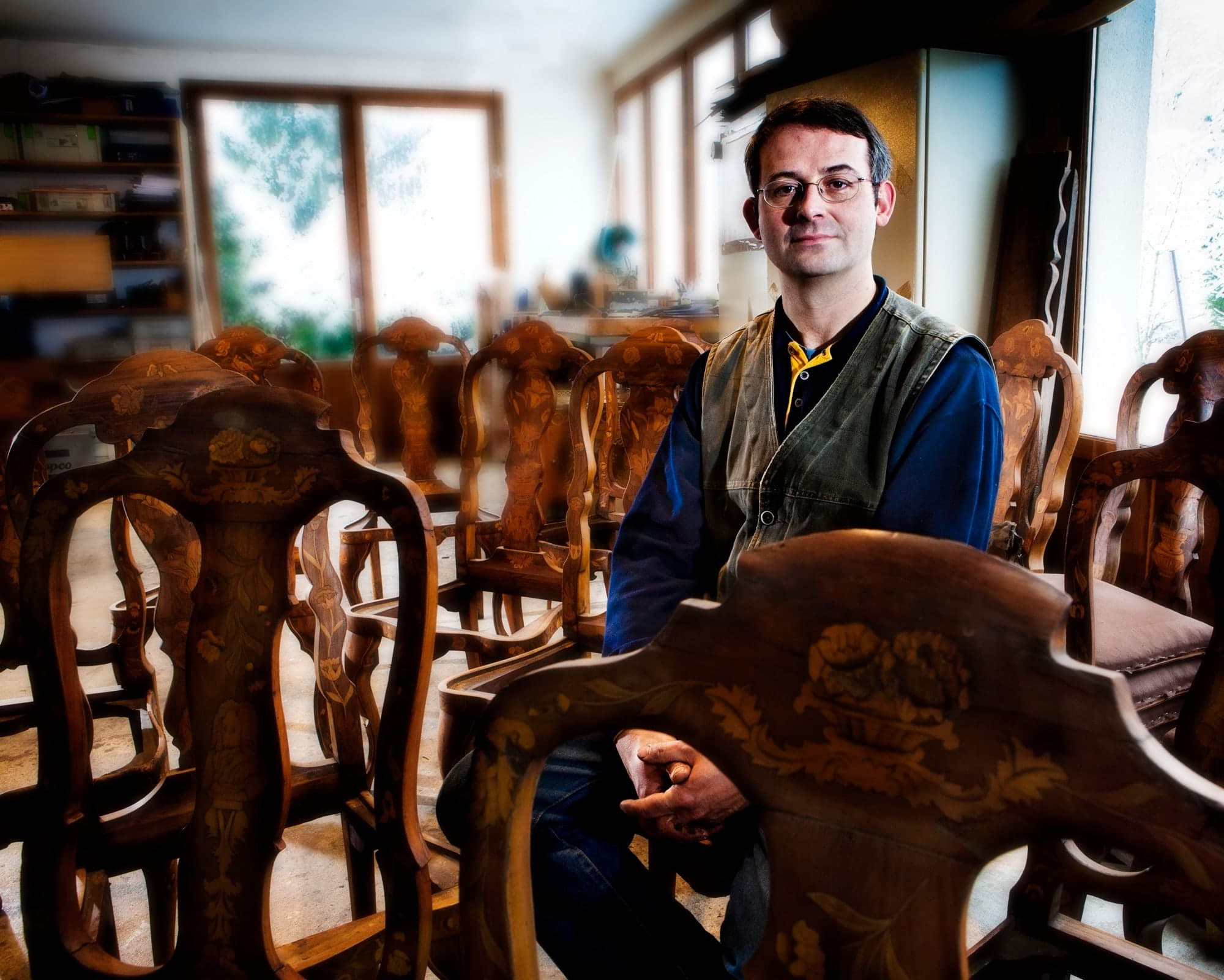portrait d'un artisan ébéniste assis au milieu d'une rangées de chaises