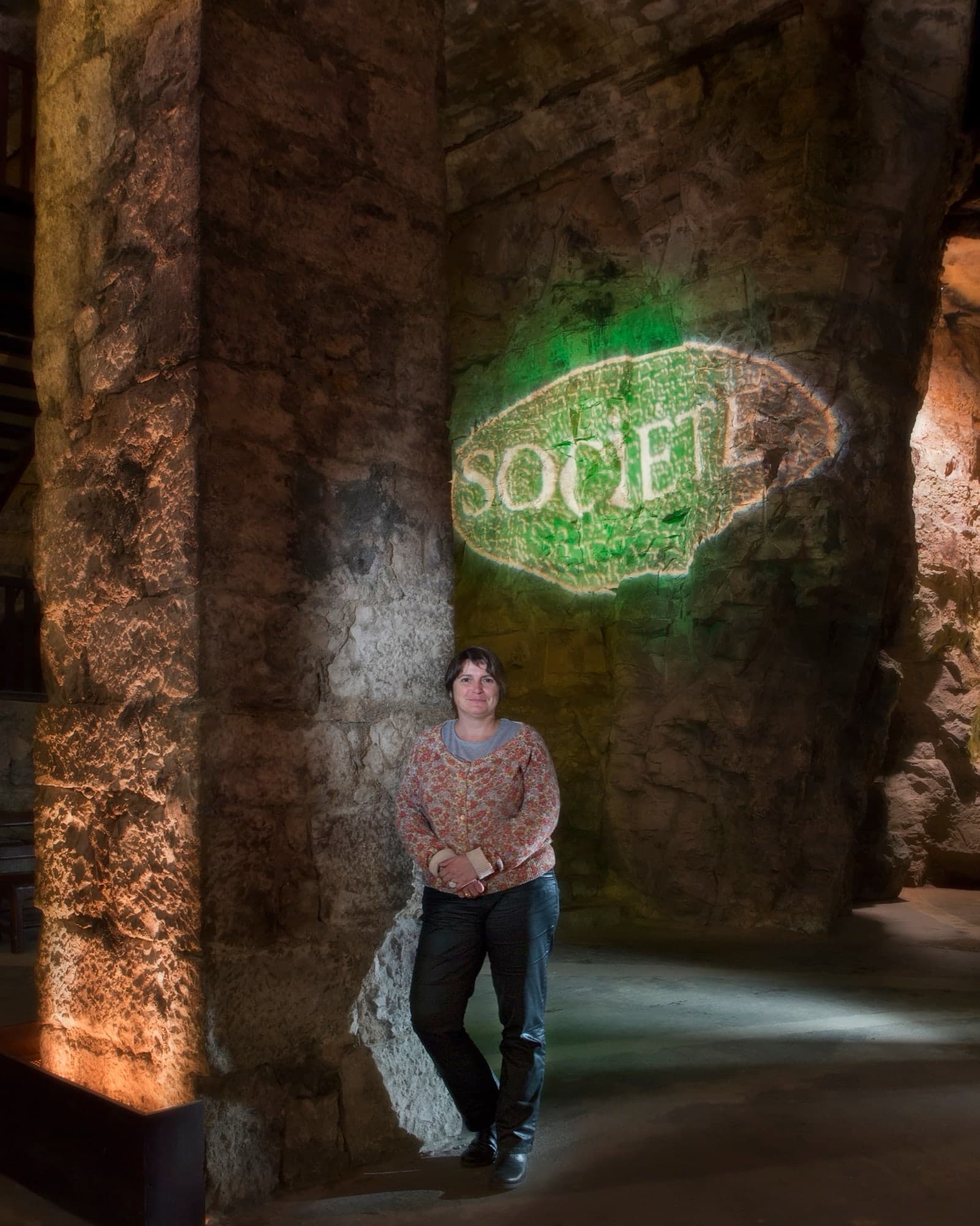 Portrait d'une femme debout dans une cave voûtée éclairée d'une enseigne verte lumineuse