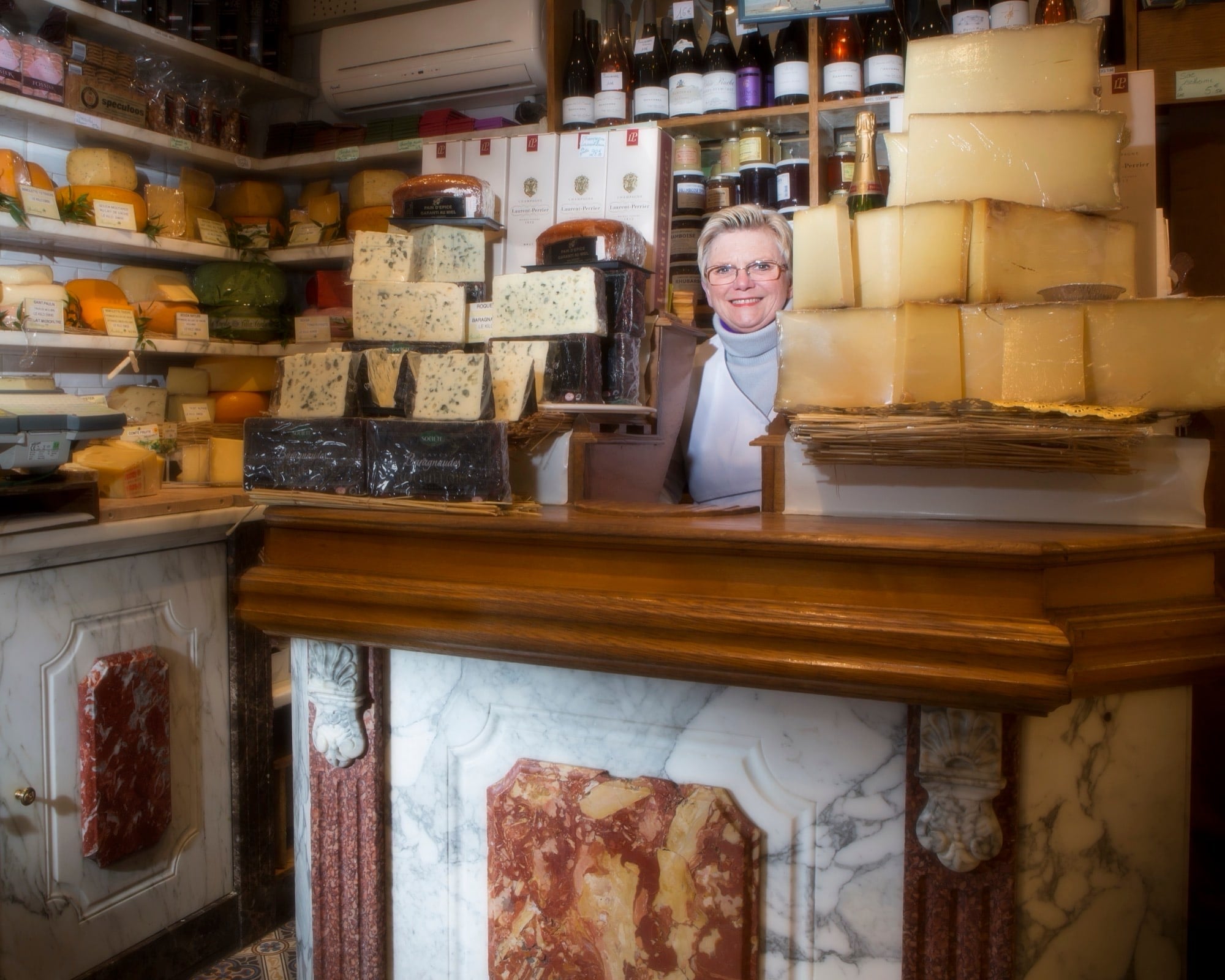 Portrait d'une fromagère derrière son comptoir en marbre entouré de fromages